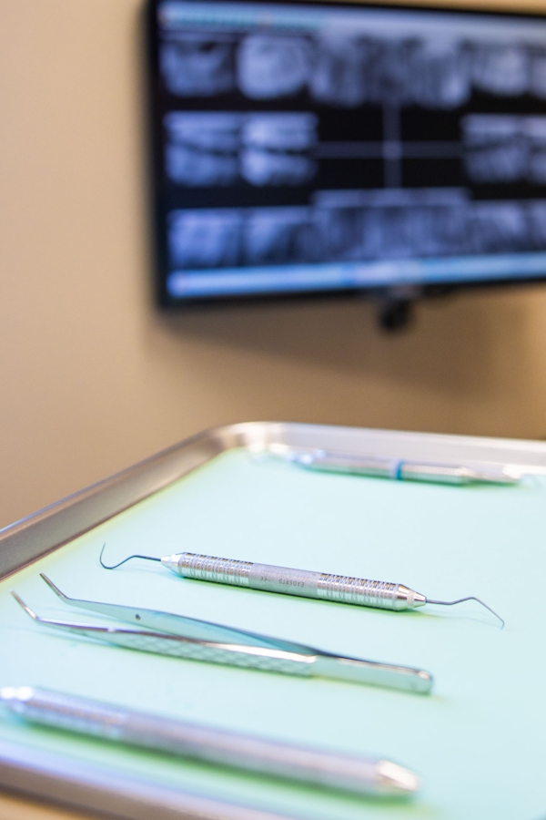 photo of dental tools on a tray with a screen in the background showing x-rays of teeth