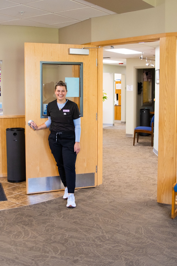 photo of a registered dental hygienist smiling and holding open a door in a dentist's office